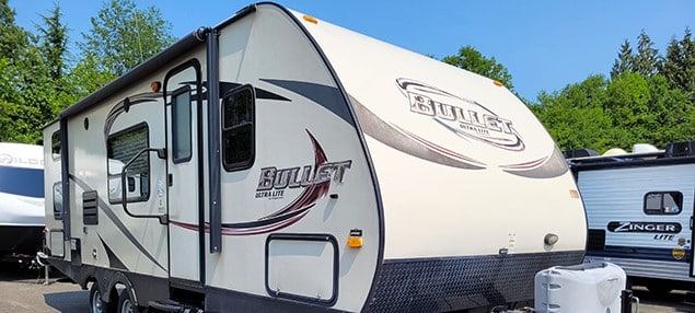 A camping travel trailer parked in a lot with other rvs near Rainbow Lake.