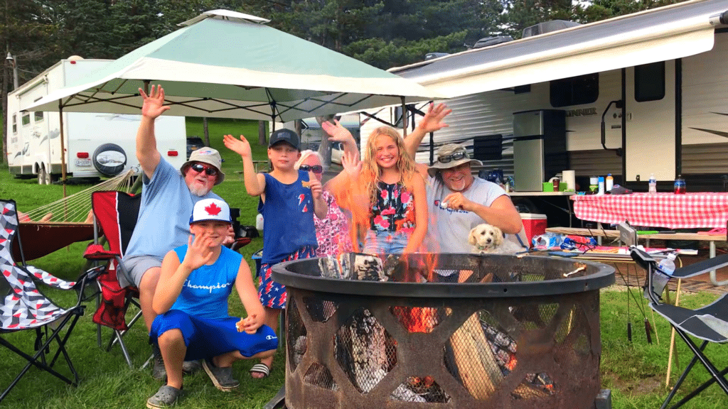 A group of people posing in front of a campfire at a campground.