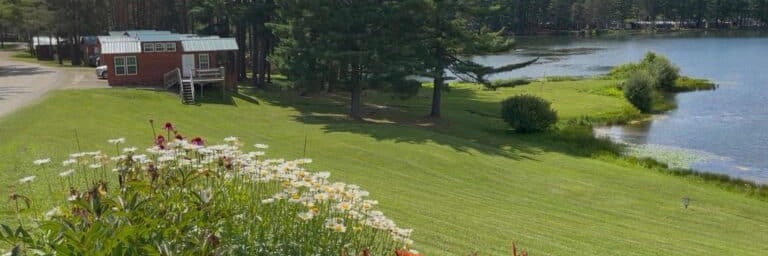 A park model cabin on the lawn above Rainbow Lake, with flower beds in front